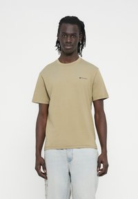 Olive green cotton t-shirt with a crew neck, short sleeves, and a small logo on the chest. Paired with light blue denim cargo shorts.