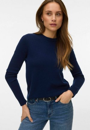 Granatowy sweter z dzianiny z długimi rękawami, okrągłym dekoltem i ściągaczami na mankietach, zestawiony z jasnoniebieskimi dżinsami i czarnym paskiem ze srebrną klamrą.