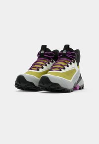 Botas de senderismo con un diseño en amarillo, negro y púrpura. Presentan una mezcla de materiales, suelas estriadas y cordones prominentes para un ajuste seguro.