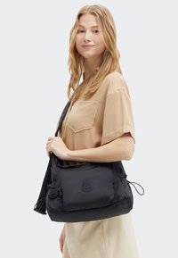 Black nylon shoulder bag with rounded shape, front pocket, and textured logo. Features adjustable strap and drawstring accent. Smooth finish.