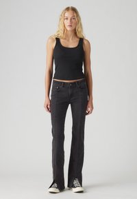Black ribbed tank top paired with black flared jeans featuring side slits, stitch detailing, and classic black-and-white sneakers.