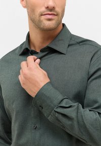 Camicia verde con bottone, dal finish testurizzato, con colletto classico, maniche lunghe e bottoni neri ai polsini e alla patta frontale.