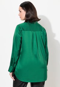Zielona satynowa koszula z długim rękawem, okrągłym kołnierzykiem i fałdą z tyłu. Gładka struktura z lekkim połyskiem, z zapinanymi mankietami.