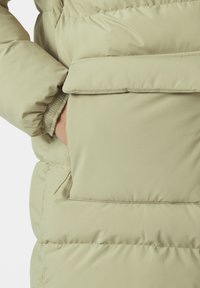 Chaquetón de plumas en beige claro con textura acolchada; cuenta con un bolsillo lateral, puños elásticos y un acabado de tejido suave.