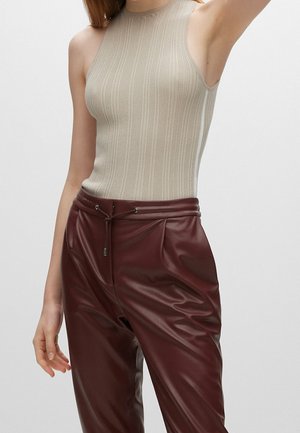Beżowy prążkowany top bez rękawów połączony z burgundowymi joggerami z sztucznej skóry, posiadającymi elastyczną talię i akcenty w postaci sznureczków.