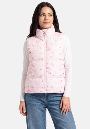 Donna che indossa un gilet imbottito rosa chiaro con motivo pupazzo di neve e cuore sopra una camicia bianca a maniche lunghe e jeans blu.