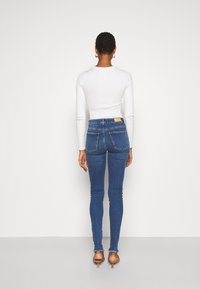Jeans justos em denim azul escuro com uma cintura alta e bainha desfiada, combinados com um top ajustado de manga longa branco.