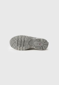 Sneaker sole with a textured gray rubber surface, featuring a wavy design and a logo emblem in the center. Durable and traction-focused.