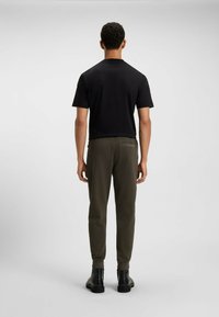 Schwarzes T-Shirt mit kurzen Ärmeln und olivgrüne Jogginghose mit elastischen Bündchen, kombiniert mit schwarzen Knöchelstiefeln, von hinten betrachtet.