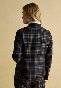 Checkered blazer in navy, green, and red. Features a high collar, textured fabric, and gold button accents. Back view shown.