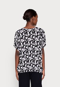 Blusa preta com padrão floral, de mangas curtas, apresentando padrões florais brancos e roxos. Corte relaxado com decote redondo e textura de tecido suave.