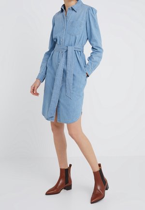 Light blue denim shirt dress with long sleeves, button closure, and matching belt. Features a chest pocket and side slits. Worn with brown ankle boots.