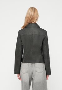 Veste en simili cuir grise avec une coupe ajustée, grand col et manches longues, associée à un jean large gris clair.