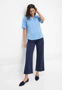 Camicia a maniche corte button-up blu chiaro abbinata a pantaloni a gamba larga blu navy e ballerine blu navy. Il tessuto appare liscio e leggero.