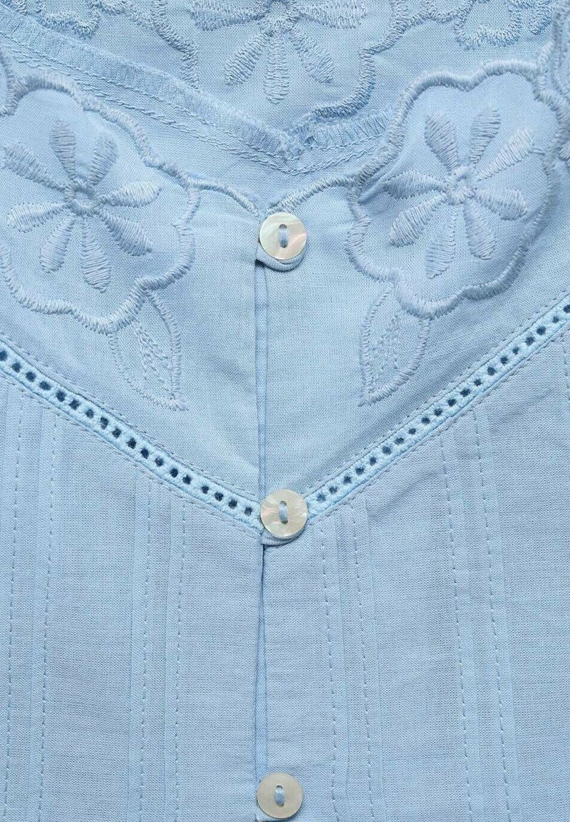 Jasnoniebieska bawełniana bluzka z haftem kwiatowym, pionowymi przeszyciami i guzikami przypominającymi perły. Skomplikowane koronkowe wykończenie wzdłuż dekoltu.