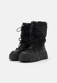 Black winter boots featuring a faux fur upper, textured rubber sole, and a chunky design with adjustable laces and cuff.