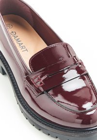 Mocasines de charol burdeos con suela plana, que presentan un acento cosido en el empeine y un acabado suave y brillante.