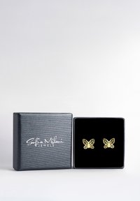 Guldörhängen i form av fjärilar visade i en svart sammetssmyckeslåda, med ett strukturerat grått lock som har varumärkets logotyp i vitt.