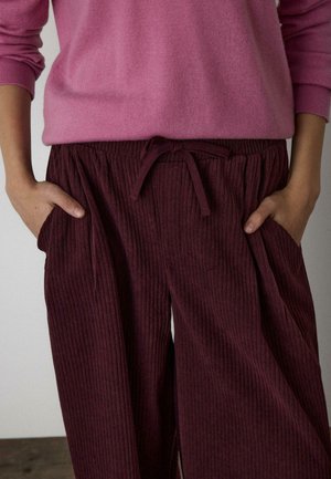 Bordové rebrované nohavice s elastickým pásom a šnúrkou, s bočnými vreckami. Kombinované s svetloružovým sveterom.