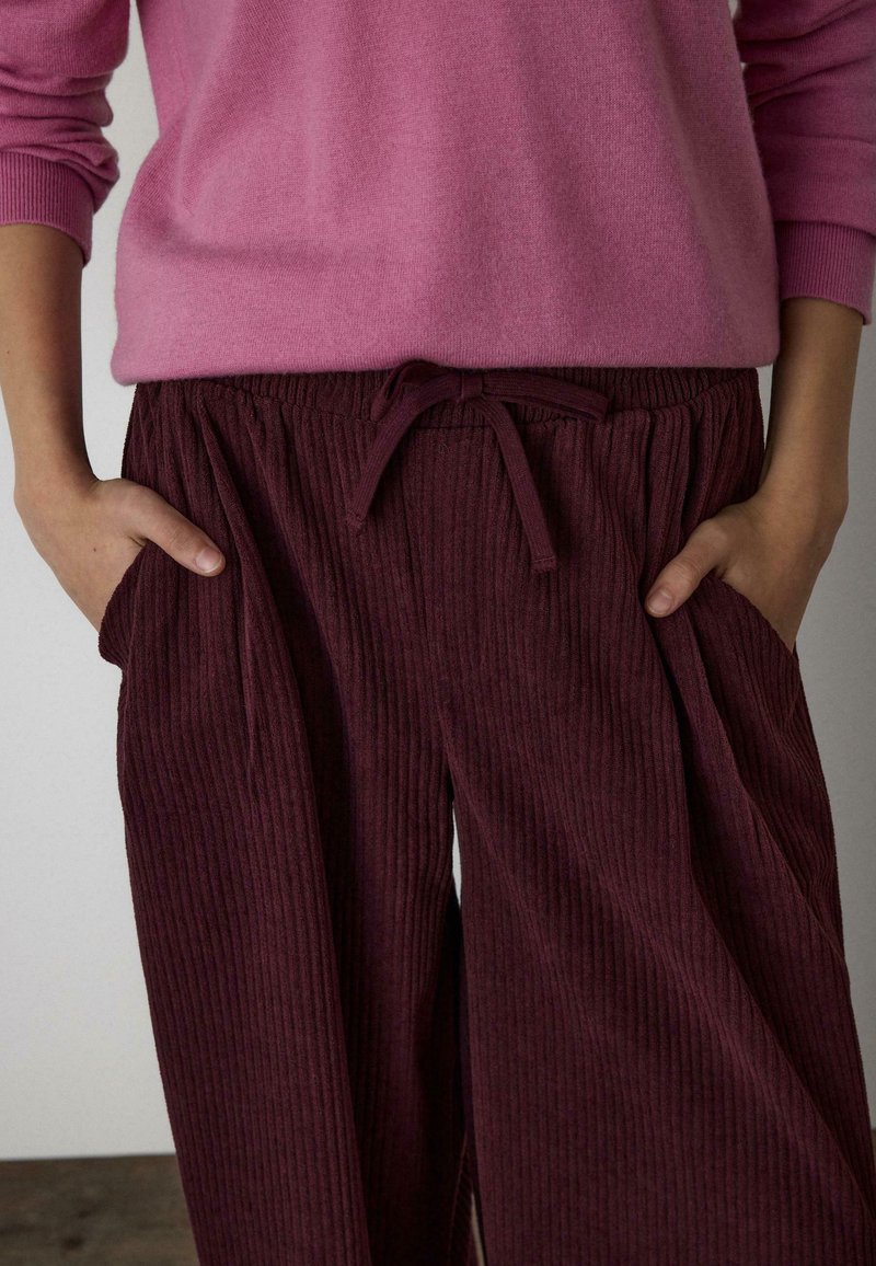 Bordové rebrované nohavice s elastickým pásom a šnúrkou, s bočnými vreckami. Kombinované s svetloružovým sveterom.
