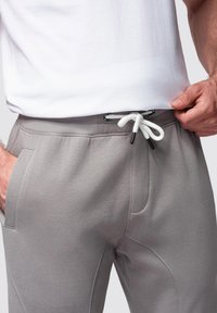 Grå mjukisbyxor med en slät yta, elastisk midja och vit dragsko. Har sidofickor och en avsmalnande design.