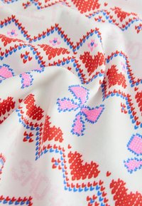 Baumwollstoff mit einem hellen Creme-Hintergrund, der ein rotes und pinkes Herzmuster zeigt, das in Blau umrandet ist, was einen strukturierten Look erzeugt.