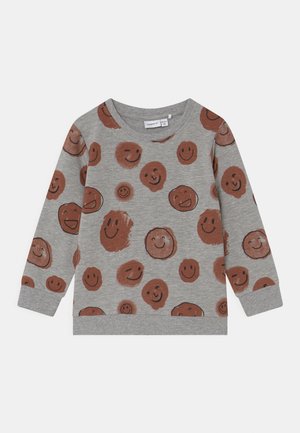 Chemise grise à manches longues avec motifs de visages souriants marron de tailles et d'expressions variées, poignets côtelés et encolure ronde.