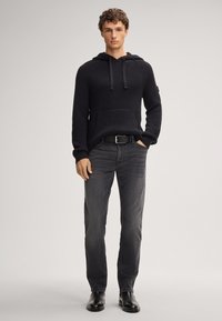 Granatowy dzianinowy hoodie z prążkowanym teksturą i kieszenią z przodu, w zestawieniu z ciemnoszarymi dżinsami i czarnymi butami, na jednolitym tle.