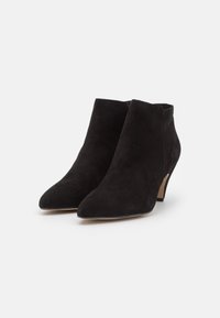 Stivaletti neri in suede con punta affilata e tacco medio, caratterizzati da una texture liscia e da un design minimalista.