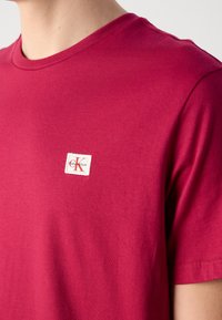 Piros pamut póló kerek nyakkal és rövid ujjakkal, a bal felső részen egy kis fehér Calvin Klein logóval ellátva.