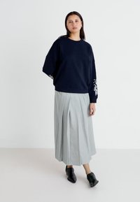Sudadera navy con diseño floral blanco en las mangas, combinada con una falda gris con pliegues y botines negros. Tejidos minimalistas y texturizados.
