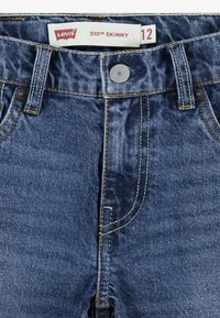 Jeans ajustados Levi's 510 en denim azul oscuro, con costuras doradas, botón delantero y diseño de cinco bolsillos. La etiqueta de tamaño indica "12".