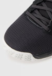 Μαύρο αθλητι�κό παπούτσι από δίχτυ με υφή, διαθέτει λευκή λαστιχένια σόλα και μαύρα κορδόνια πάνω σε λεία μαύρη υφασμάτινη γλώσσα.