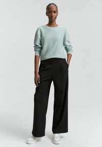 Šviesiai žalia tekstūruota megzta palaidinė ir plačios juodos kelnės, derinamos su baltomis sportinėmis bateliais. Apranga pasižymi laisvu siluetu ir minimalistiniu dizainu.