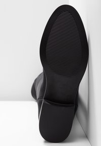 Calzado negro con una parte superior lisa y una suela de goma texturizada, con punta redondeada y un tacón cuña bajo.