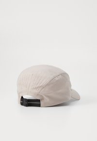 Beige cap with a structured design, featuring perforated details on the crown and an adjustable black strap at the back.