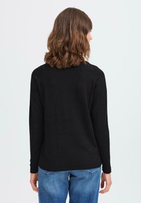 Svart langermet genser laget av mykt materiale, med rund halslinning og rett nederkant, sammen med lyseblå denimjeans.