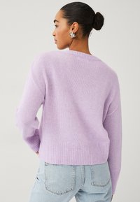 Pull en maille lavande avec ourlets et poignets côtelés. Texture douce, coupe décontractée et encolure arrondie dans le dos. Associé à un jean bleu clair.