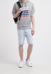 Sudadera corta gris con mangas cortas y gráfico de estrellas y rayas, combinada con pantalones cortos de mezclilla azul claro. Zapatillas blancas y mochila negra.