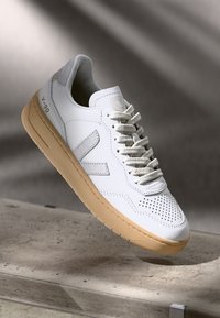 Witte leren sneaker met geperforeerde details, beige rubberen zool en lichtgrijze accenten; heeft een traditionele vetersluiting.