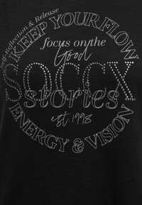Black fabric with circular silver text, "KEEP YOUR FLOW Self-Reflection & Release, focus on the good, SOCIETY stories est. 1998, ENERGY & VISION."