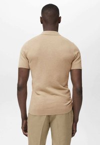 Polo shirt beige a maniche corte con orlo dritto, realizzato in tessuto a maglia testurizzata. Dettaglio del colletto semplice e silhouette aderente.