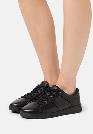 Baskets basses en cuir noir à lacets portées pieds nus, vues de profil avant sur un fond uni.