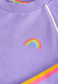 Lila pamut pulóver szivárvány hímzéssel rózsaszín, sárga, zöld és kék színekben, fehér dísztűzéssel és bordázott nyakkal.