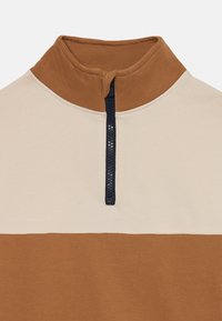 Halv-zip genser med et beige og brunt fargeblockdesign. Laget av mykt stoff; har høy krage og kontrasterende marineblå glidelås.