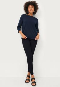 Marineblaues Langarmshirt mit lockerer Passform, kombiniert mit schwarzen Skinny-Hosen und schwarzen Riemchensandalen. Glattes Material, schlichtes Design.