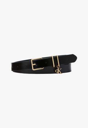 Cinturón de cuero negro con hebilla dorada y dos anillas, con colgante dorado "ck" y logo Calvin Klein en relieve cerca del extremo puntiagudo.