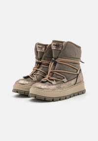 Des bottes grises et dorées métalliques disposent d'un collier rembourré, d'un système de laçage à l'avant et d'une semelle en caoutchouc texturée avec des crampons profonds pour une meilleure adhérence.