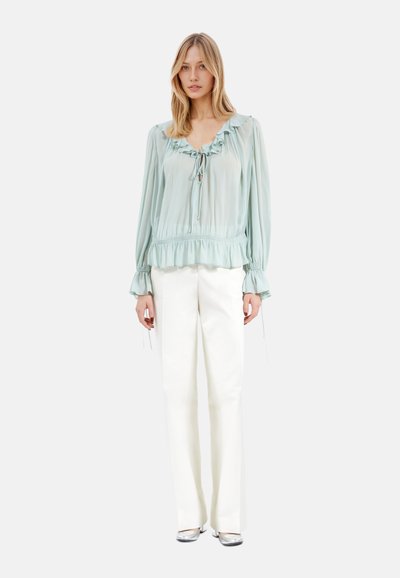 Blusa verde menta chiaro con colletto e polsini arricciati, dettagli con coulisse e orlo arricciato, abbinata a pantaloni bianchi a gamba larga.