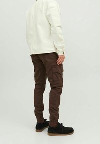 Giacca di denim bianca, pantaloni cargo marroni, scarpe nere con tomaie texturizzate e suole in gomma. Tasche visibili sui pantaloni.